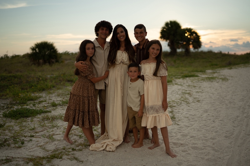 dark dull image before editing, a mother is surrounded and embraces her 5 children, three sons, and two daughters at the beach