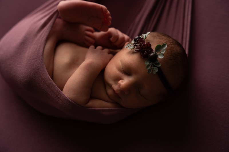 dark dull image before editing, a baby lays sleeping swaddled in blankets, she wears a little floral headband