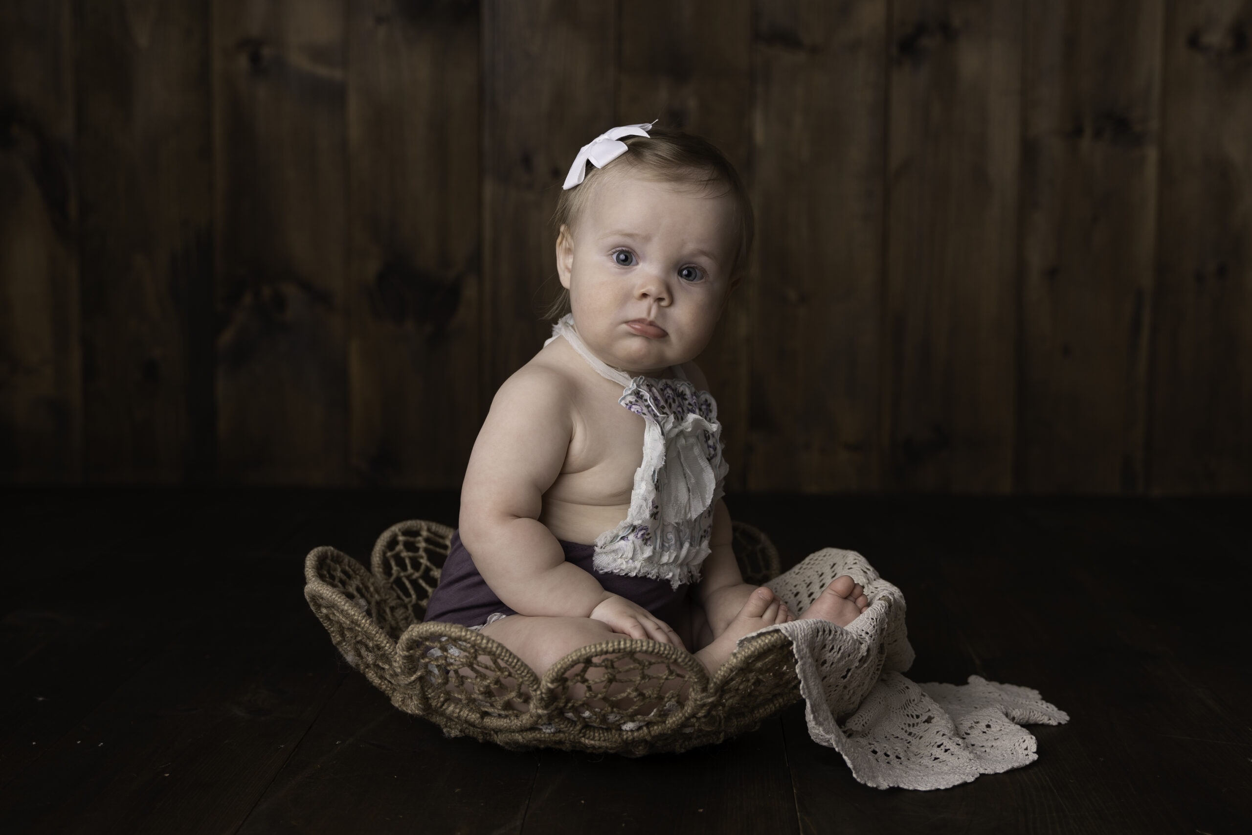 Dark Image, a baby girl sits up in a small wicker basket