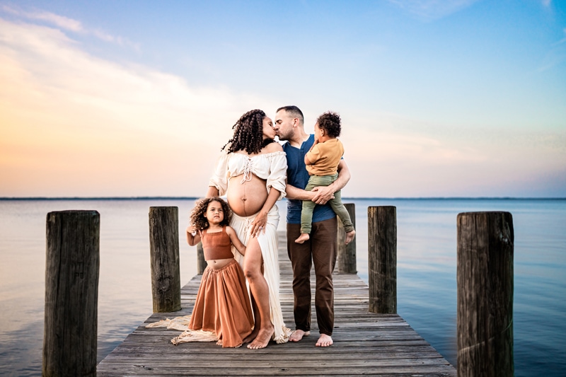 Mom and dad kiss as they hold onto their two children, on an ocean pier