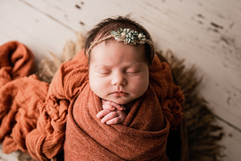 Moor Preset Pack, a lightened and edited image, a baby lays sleeping swaddled in woven blankets, a flower headband in her hair